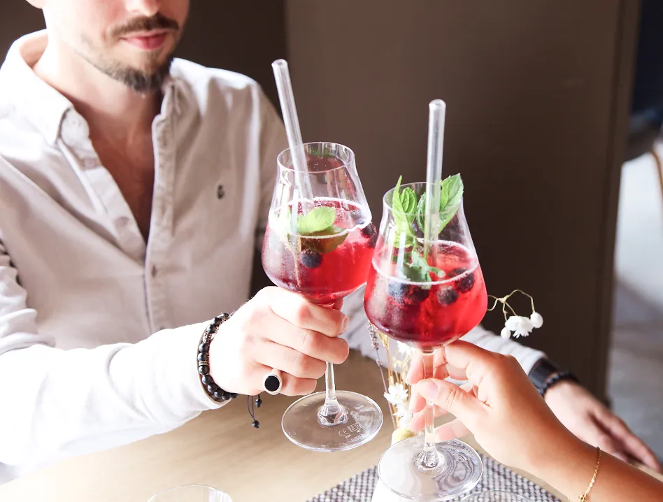 Two people toasting with red berry cocktails garnished with mint and blueberries, on a wooden table.